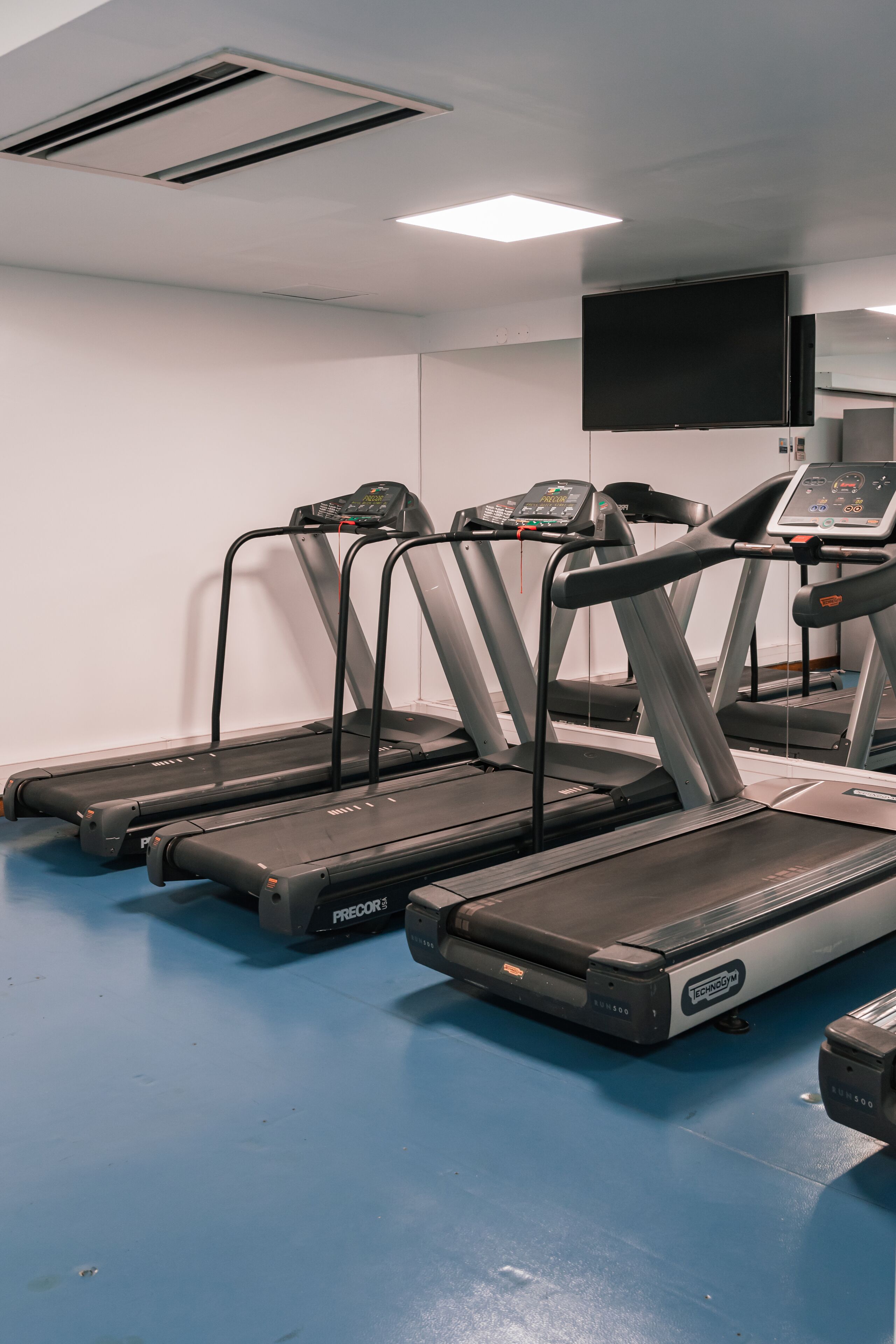 A fitness room with treadmills, a large mirror, and a flat-screen TV.