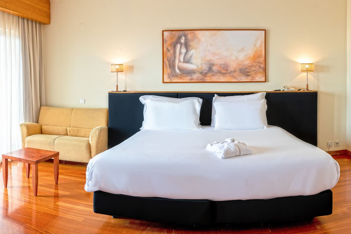 Une chambre d’hôtel avec un grand lit, un canapé, une petite table et deux lampes de chevet.