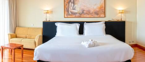 A hotel room with a large bed, a sofa, a small table, and two bedside lamps.