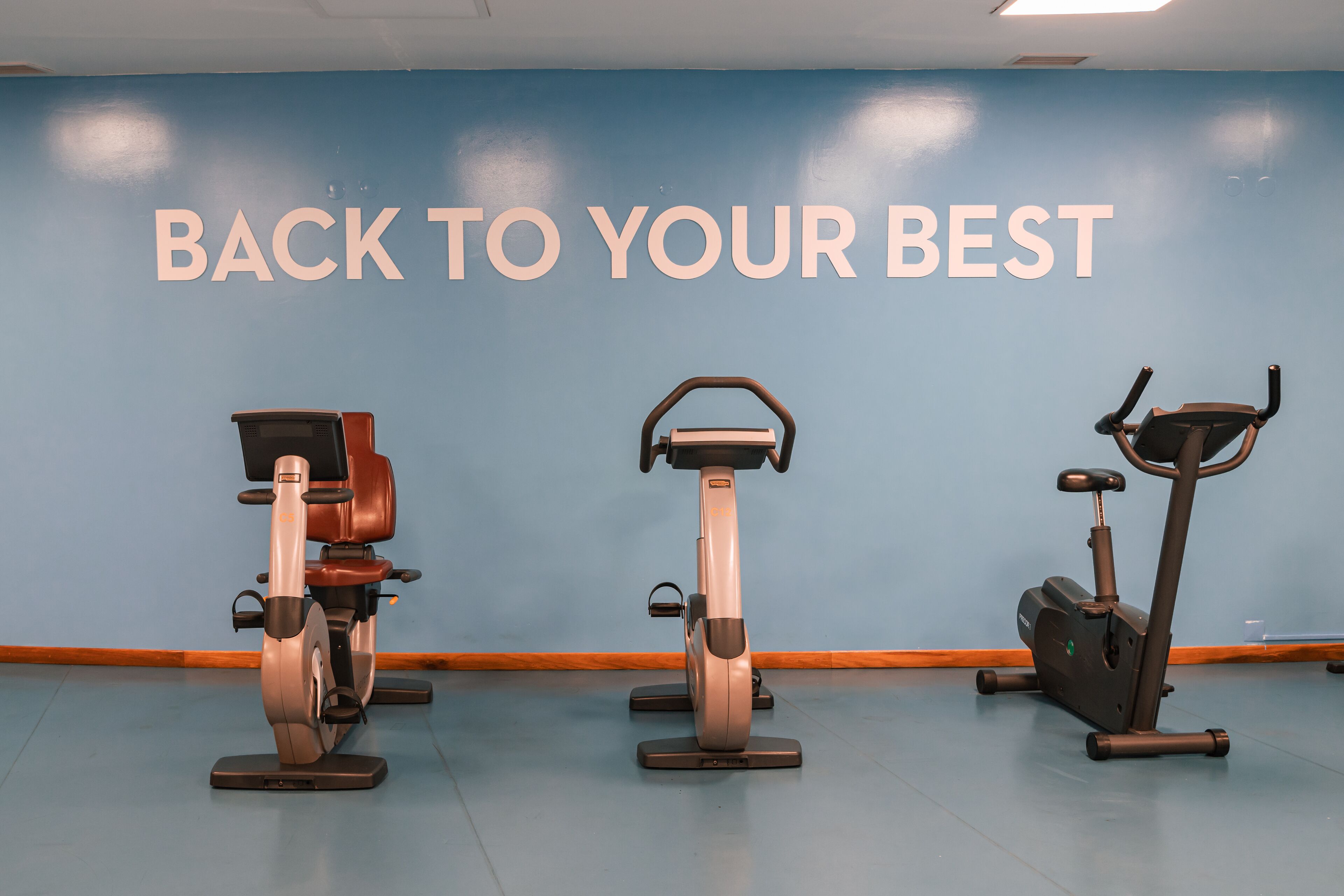 Three stationary bikes in a room with a blue wall and the text "BACK TO YOUR BEST".