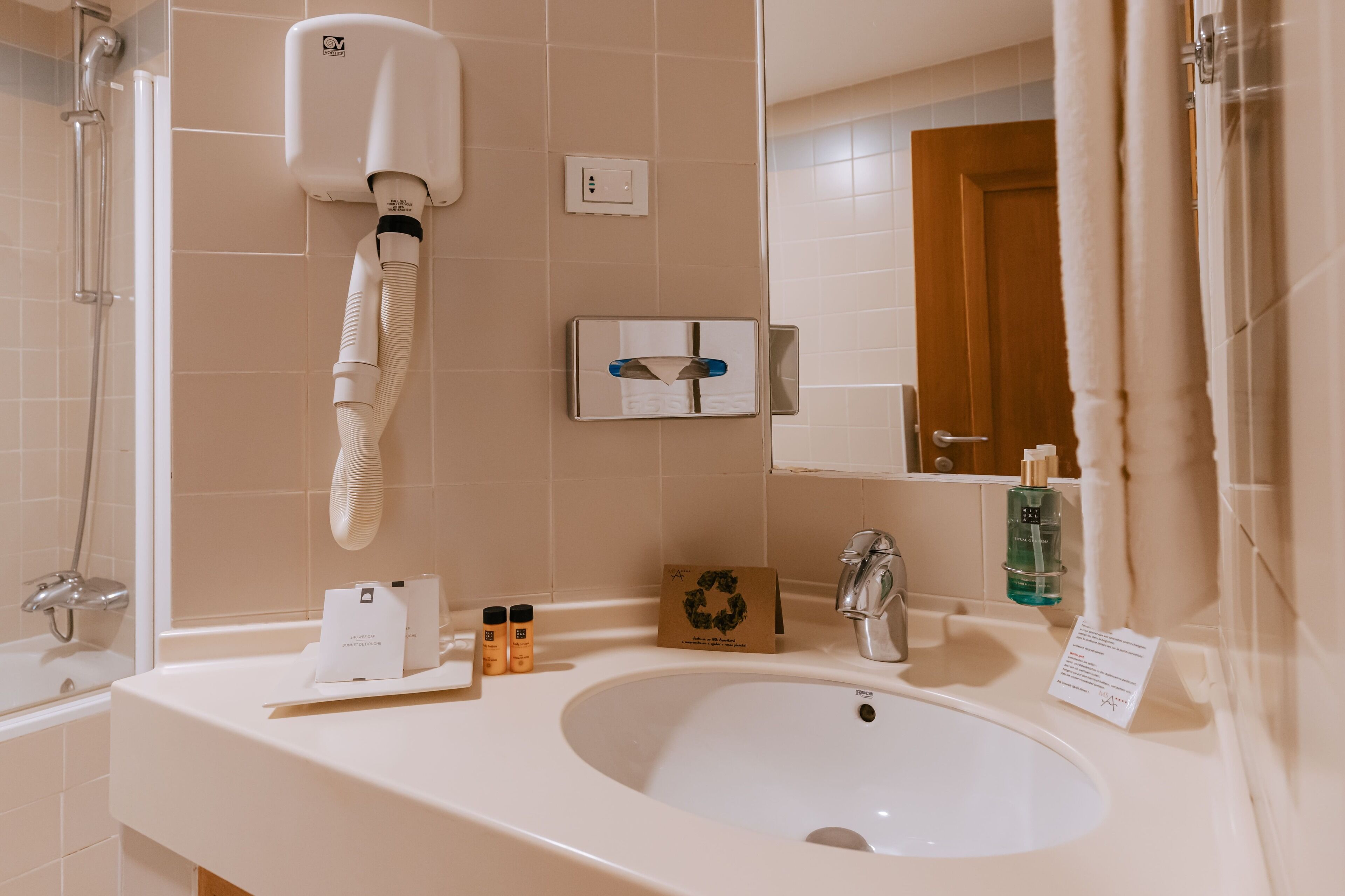 Een badkamer met een wastafel, spiegel, handdoekdispenser en douche.