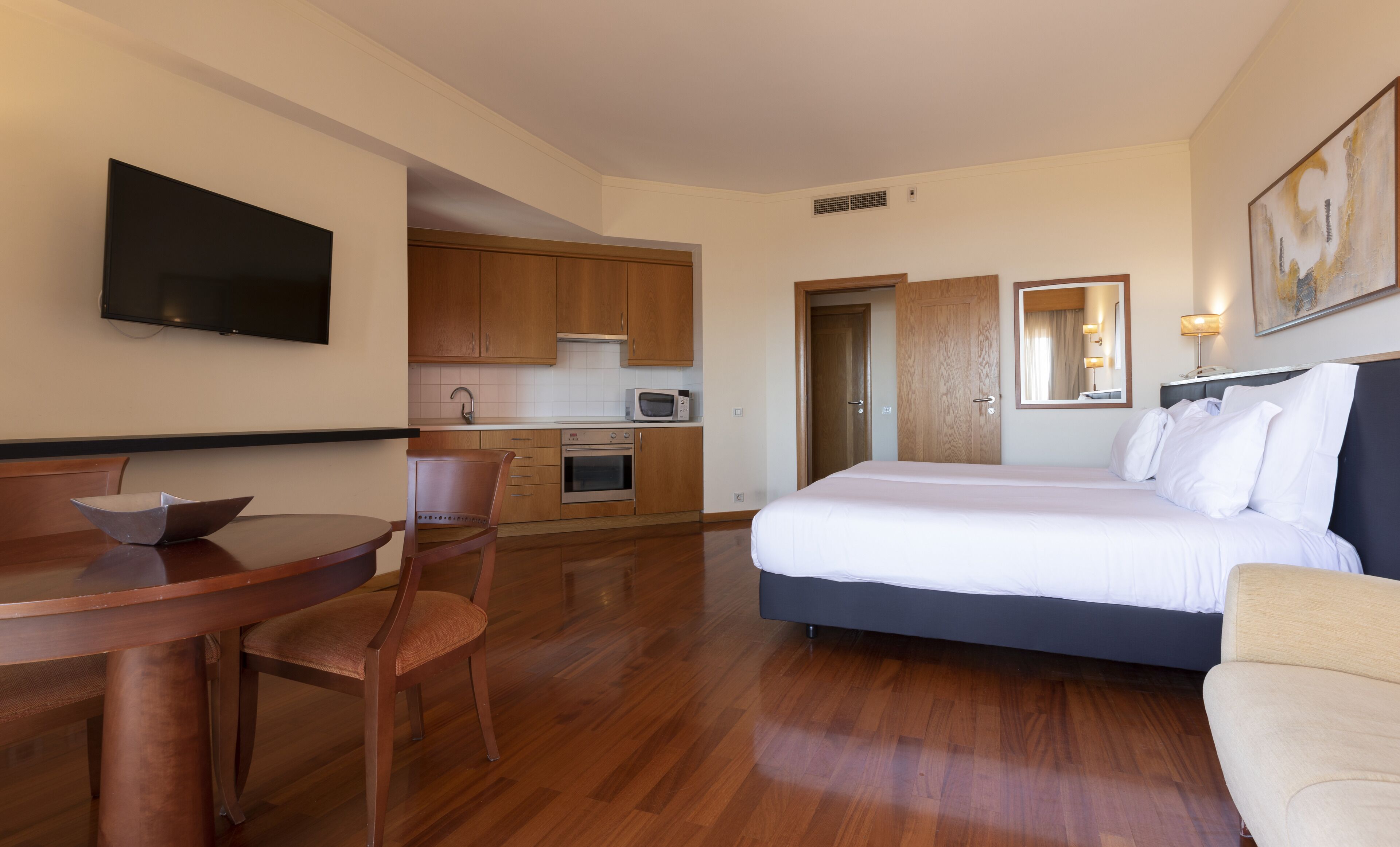 Una habitación de hotel con cama, escritorio, silla, kitchenette y televisor.