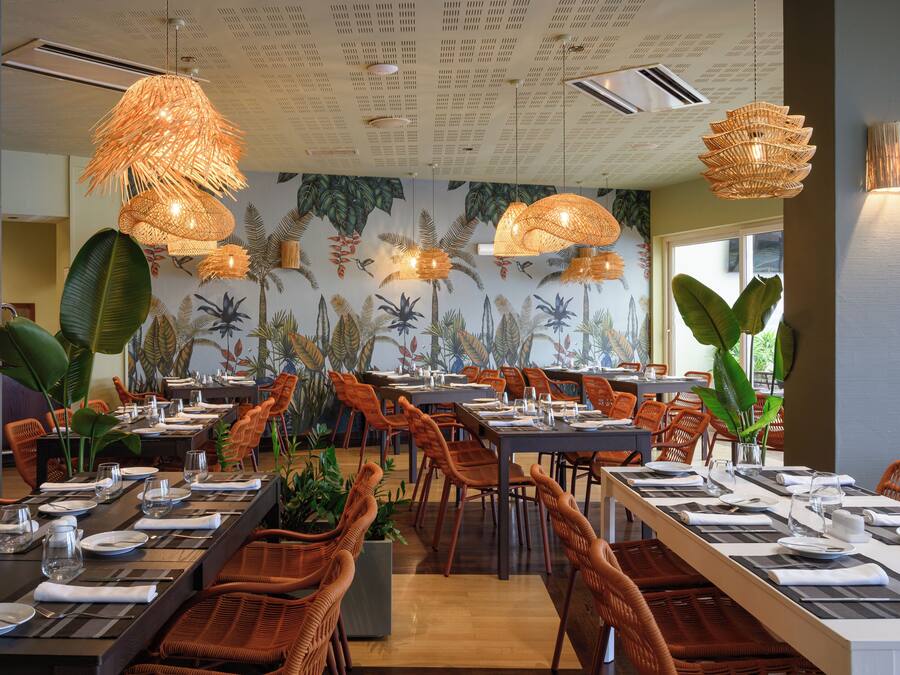 Ein Restaurant mit langen Gemeinschaftstischen, Korbstühlen und hängenden Lampen aus Korbgeflecht.