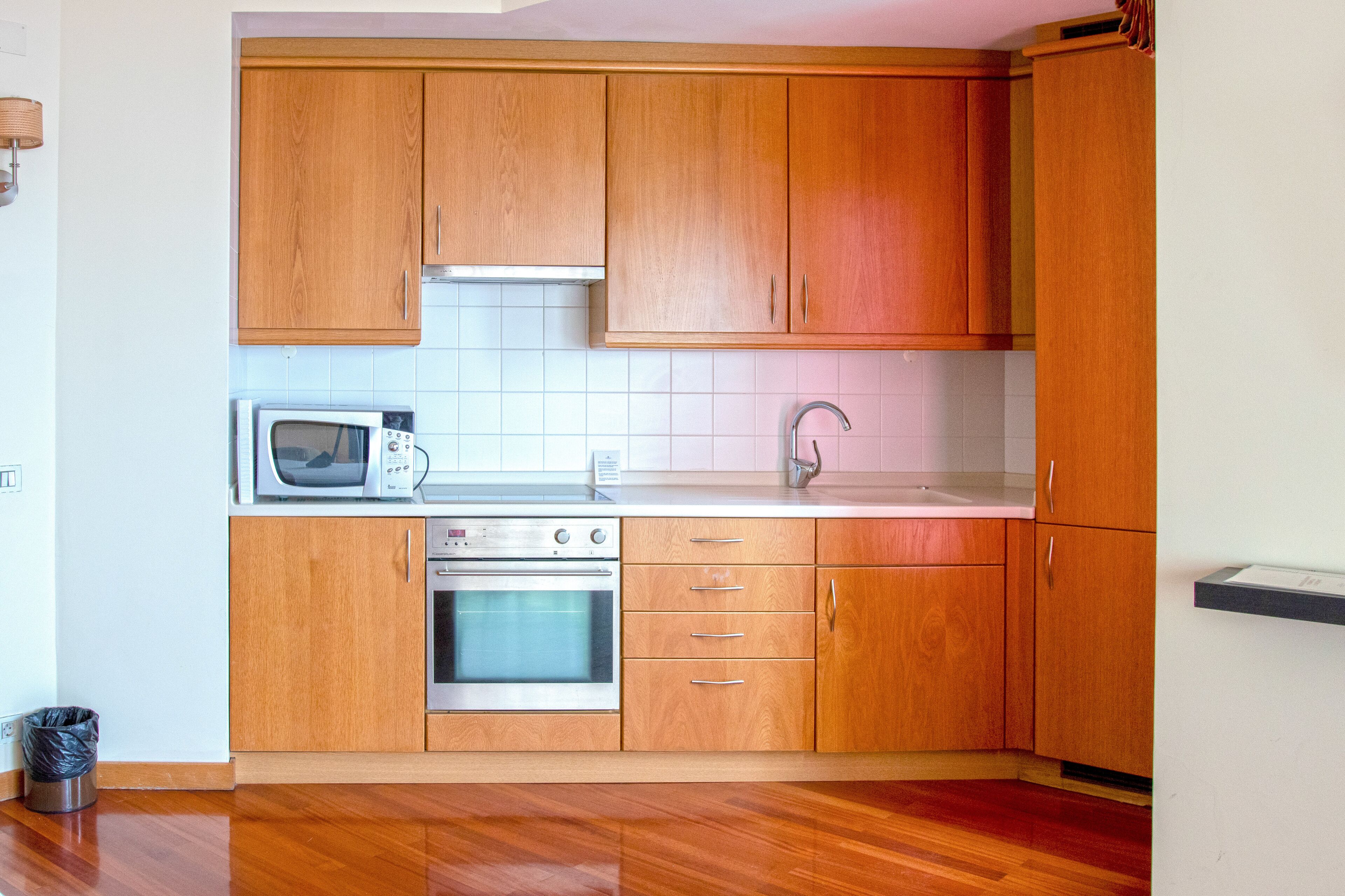 Een kleine keuken met houten kastjes, een magnetron, een oven en een spoelbak.