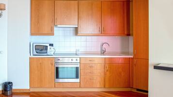 Een kleine keuken met houten kastjes, een magnetron, een oven en een spoelbak.