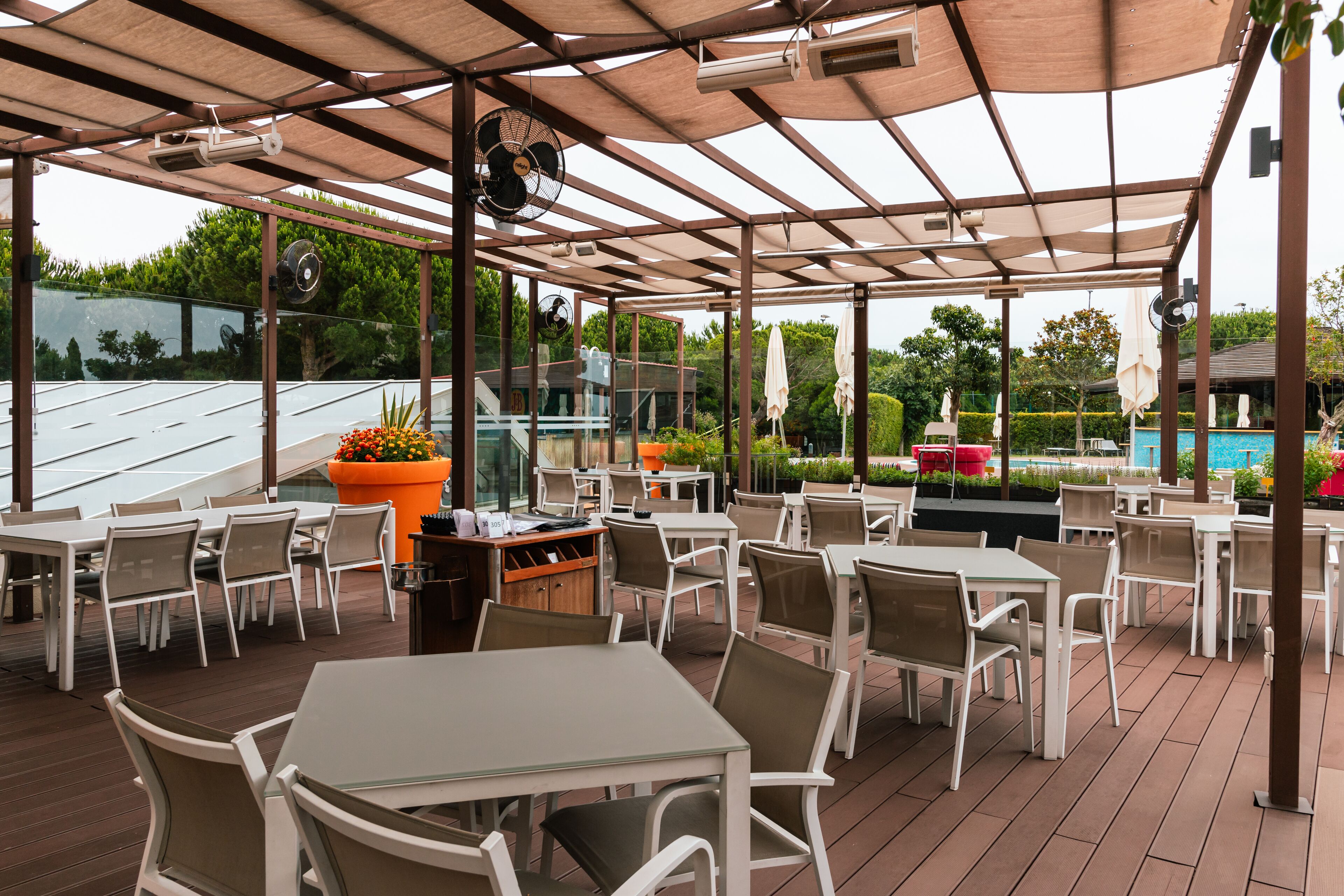An outdoor patio area with tables and chairs, a pool, and a covered section with a fan.