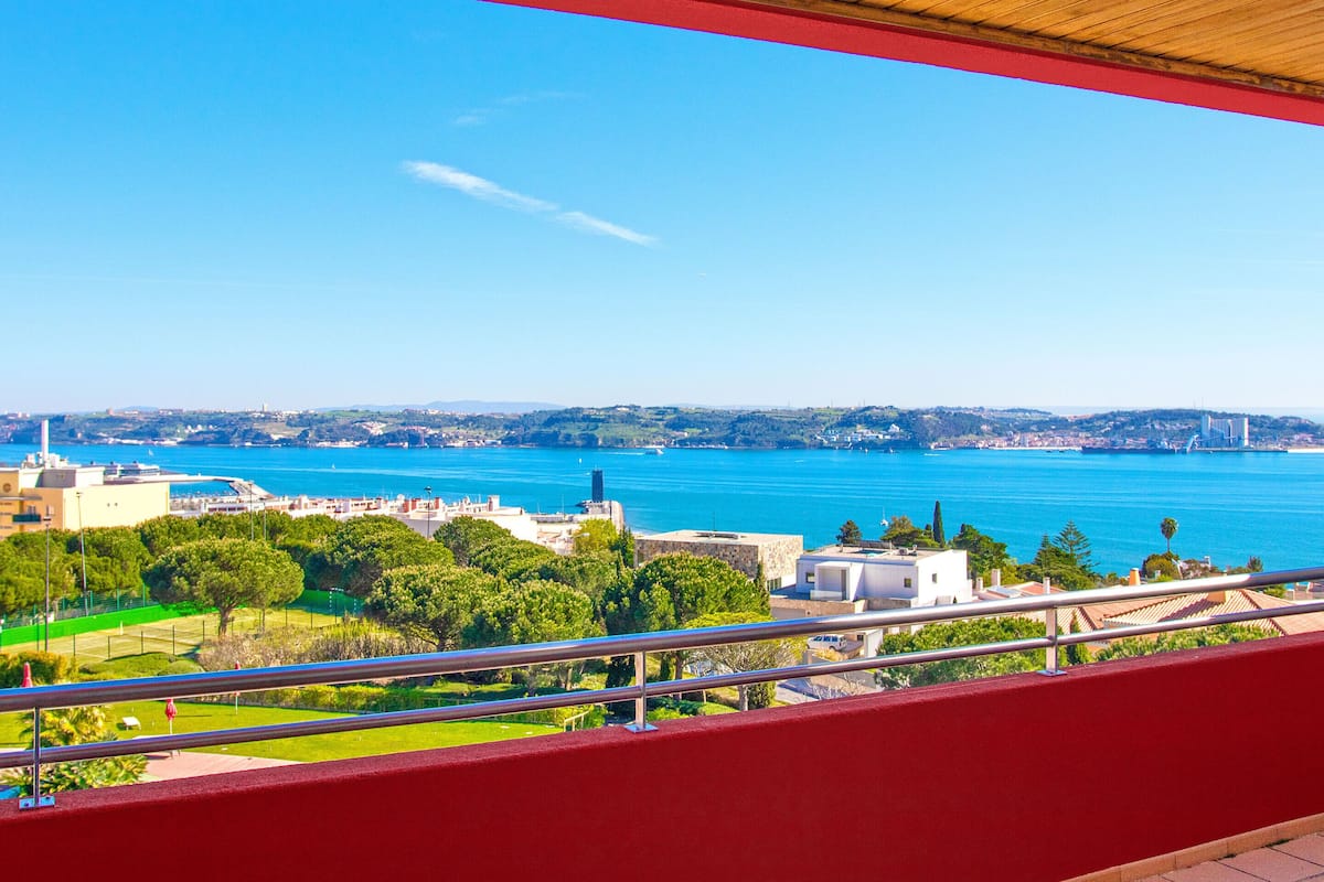 Un balcon offrant une vue sur un paysage urbain côtier, avec un pont et une vaste étendue d’eau.