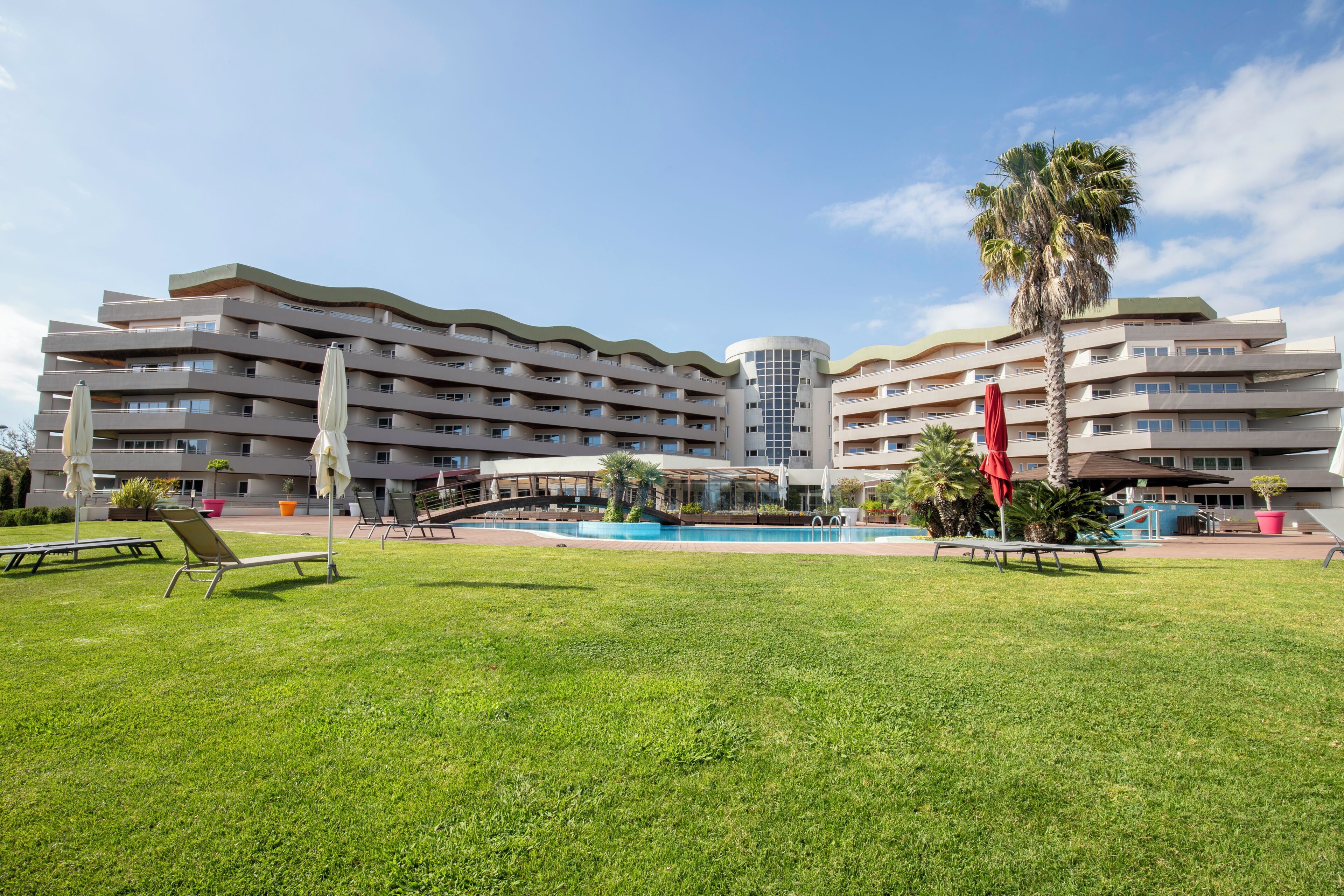 Un hôtel à plusieurs étages doté d’une piscine, d’un espace extérieur aménagé et de palmiers.
