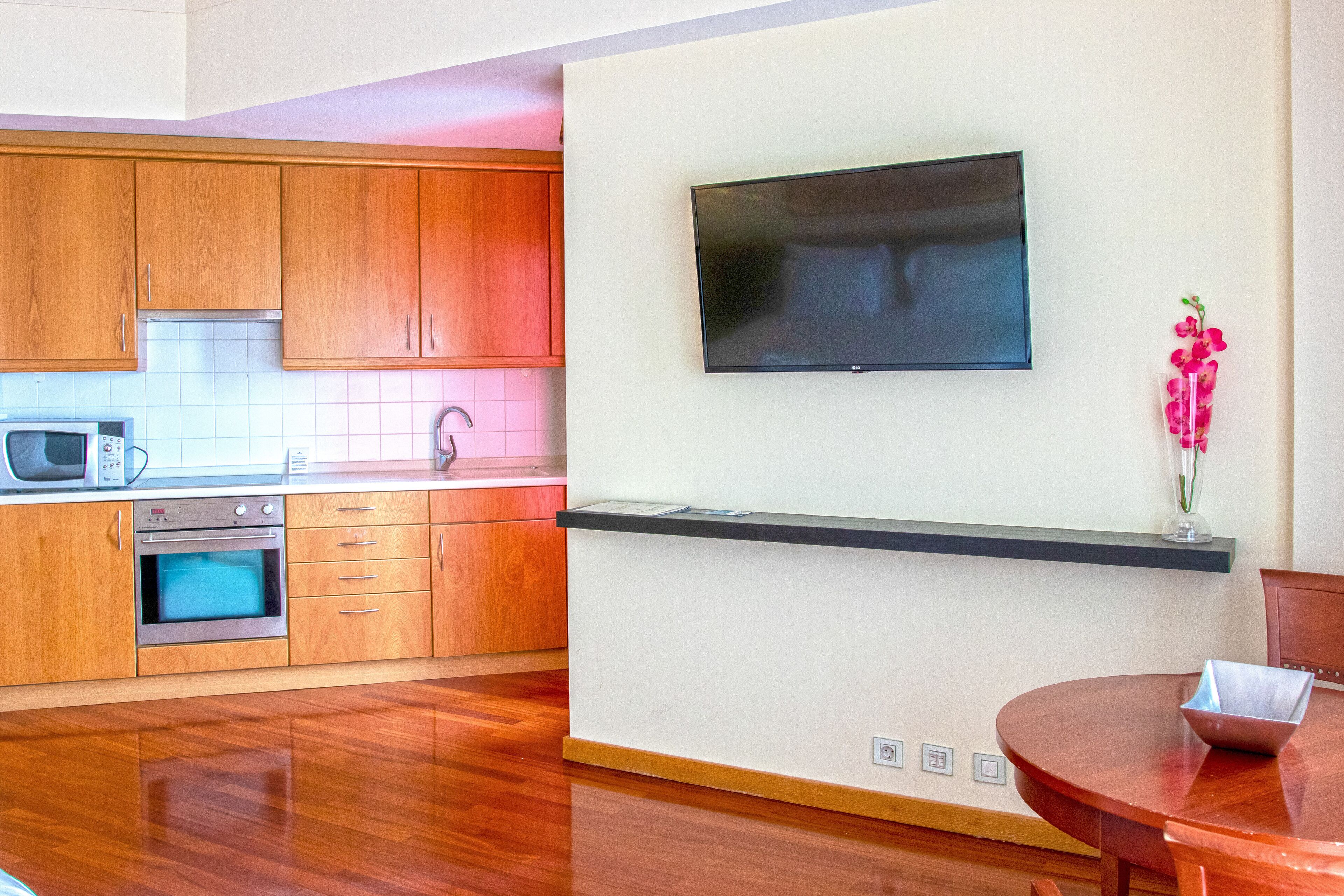 Una cocina moderna con armarios de madera, microondas, horno y televisor de pantalla plana montado en la pared.