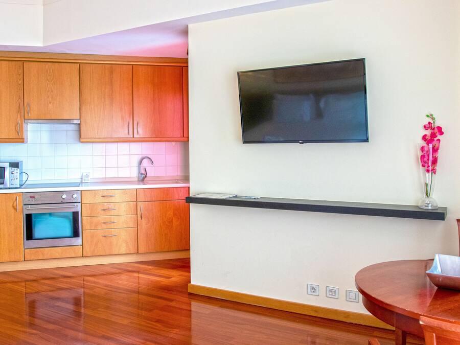 Una cocina moderna con armarios de madera, microondas, horno y televisor de pantalla plana montado en la pared.