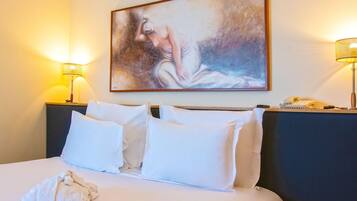 A hotel room with a bed, two bedside lamps, a painting on the wall, and a telephone on the nightstand.