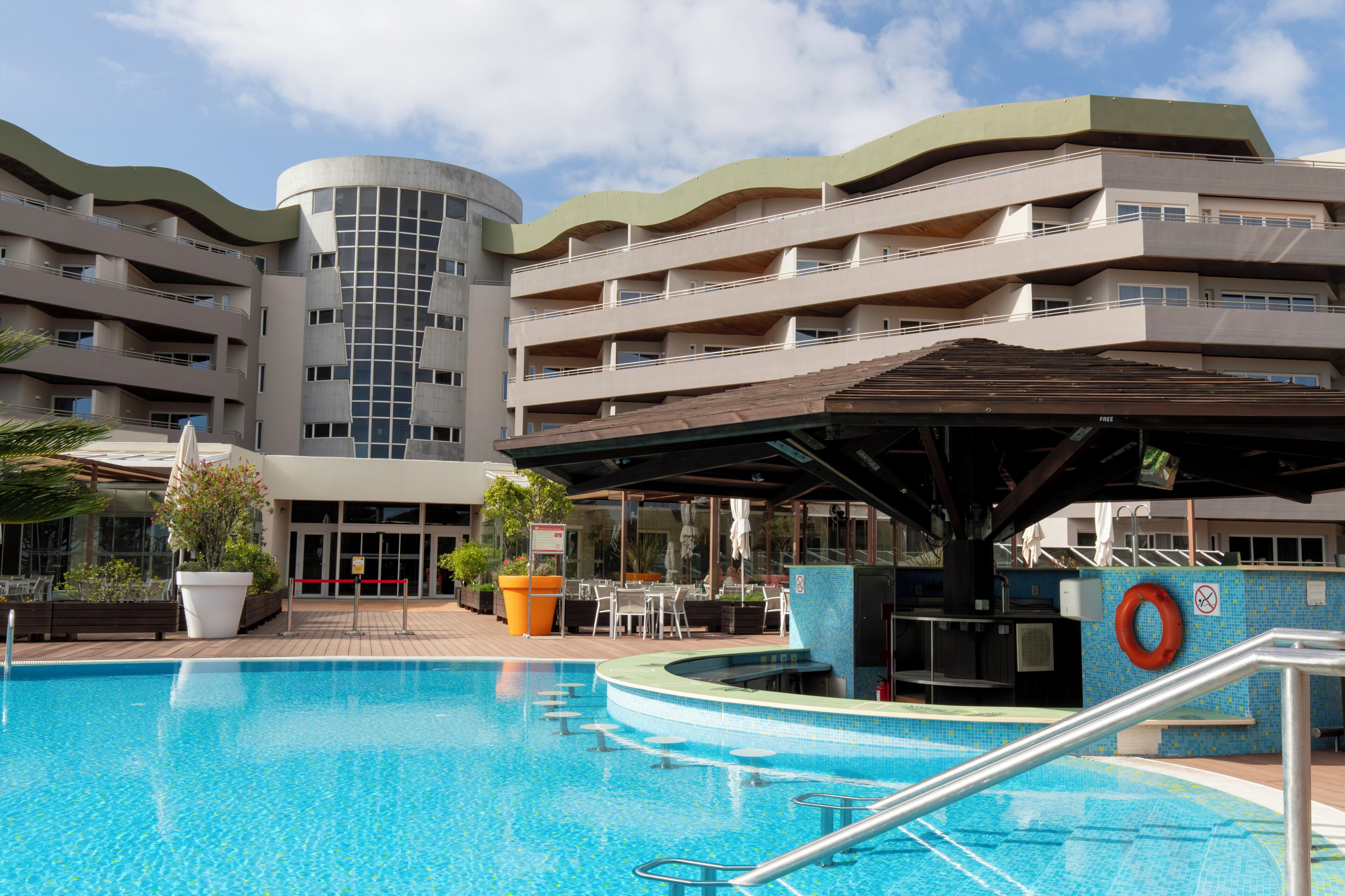 A swimming pool with a covered area, a lifebuoy, and a building with multiple balconies.