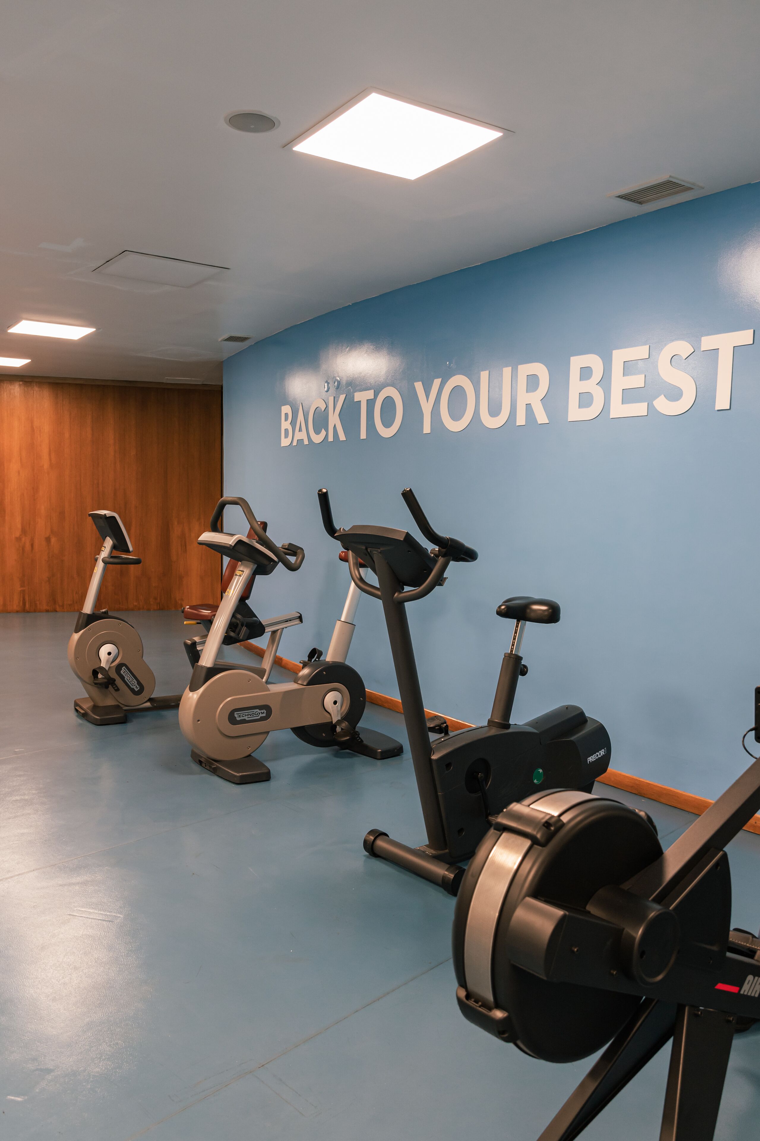 Un gimnasio con tres bicicletas estáticas y una pared con texto motivacional.