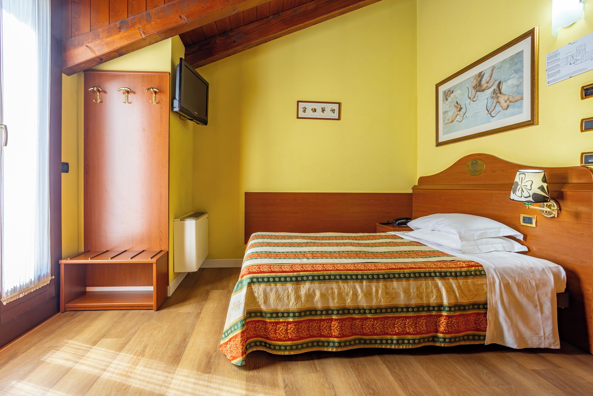 A hotel room with a bed, a wooden headboard, a television, and a painting on the wall.