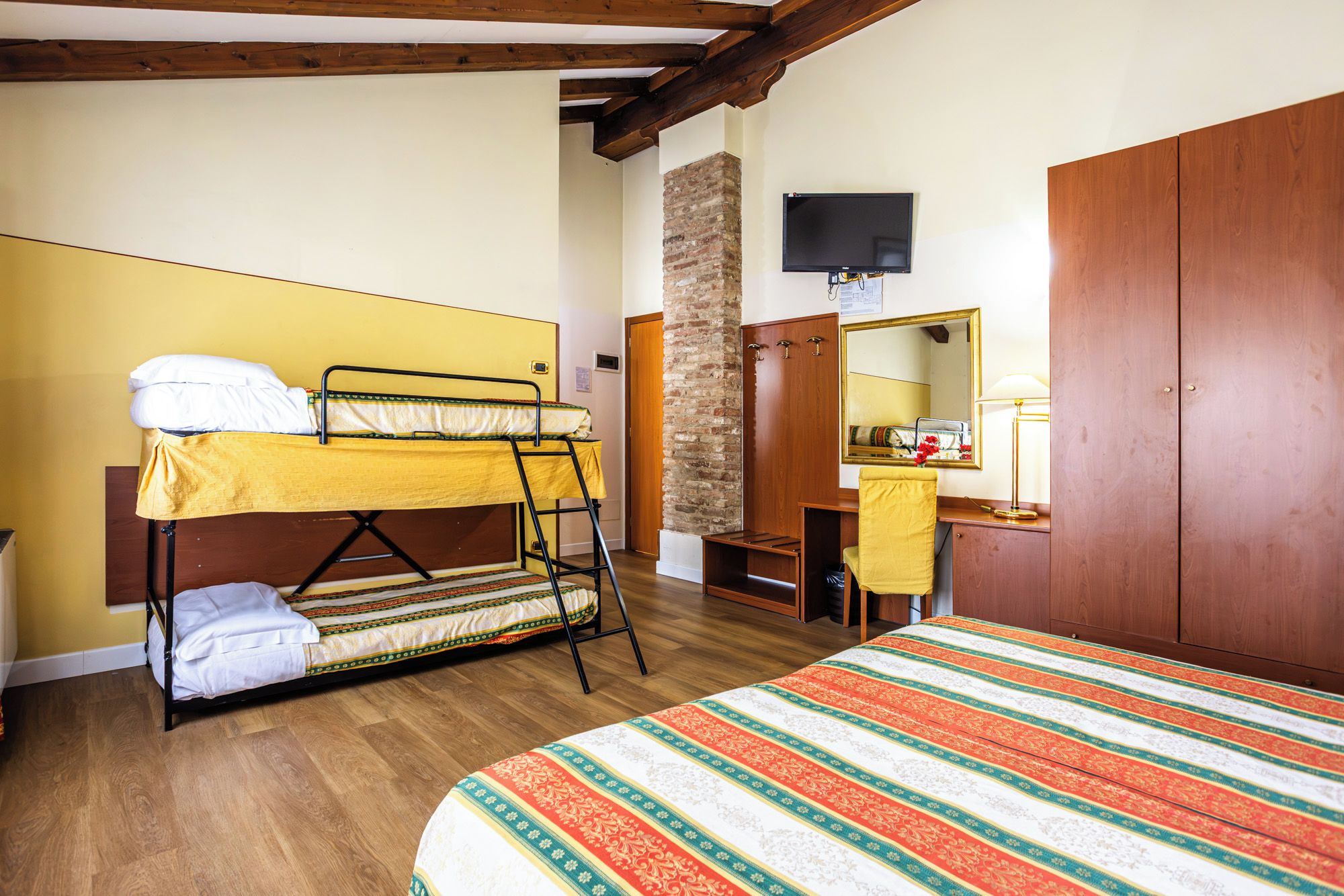Quarto com beliche, guarda-roupa de madeira, escrivaninha com cadeira e espelho.