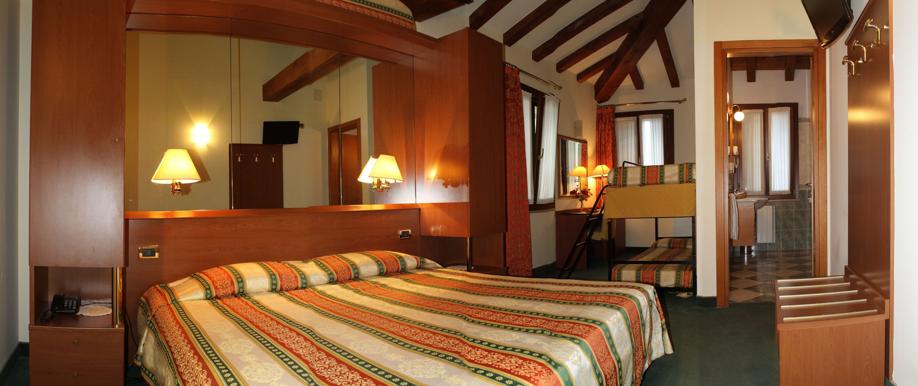 Ein Hotelzimmer mit einem großen Bett, einem Schreibtisch mit Lampe, einem Spiegel und einer Treppe, die in ein weiteres Zimmer führt.