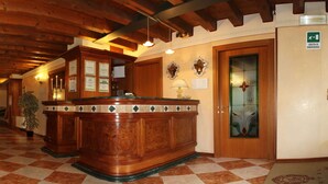 A lobby with a checkered floor, wooden reception desk, and a reception area with a green emergency exit sign. - Hotel Antico Moro (Mestre)