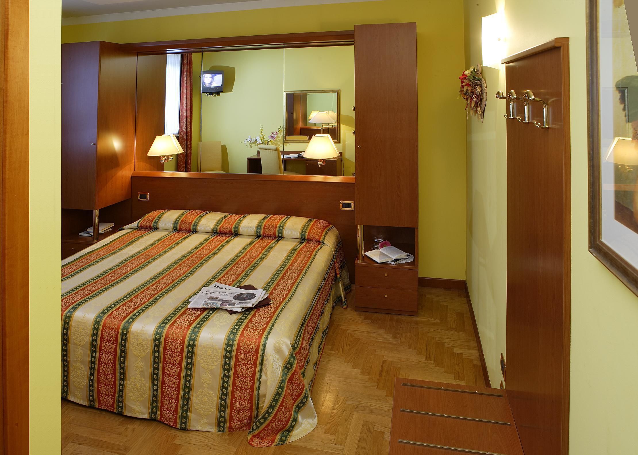 A hotel room with a large bed, a wooden wardrobe, a mirror, and a television.