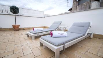 Terraço no telhado com duas espreguiçadeiras, uma planta em vaso e uma parede branca.