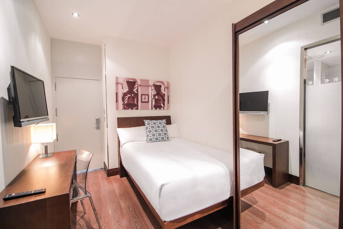 Une chambre d’hôtel avec un lit, un bureau avec une lampe, une télévision et un miroir.