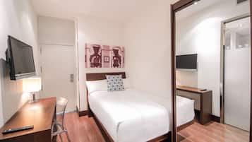Habitación de hotel con cama, escritorio con lámpara, televisor y espejo.