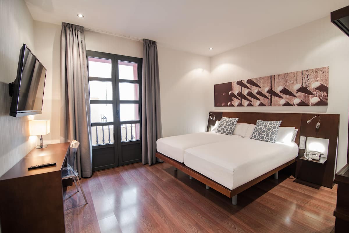 Une chambre d’hôtel avec un lit, des tables de chevet, une télévision et une fenêtre avec des rideaux.
