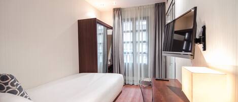 Habitación de hotel con cama, escritorio, televisor montado en la pared y ventana con cortinas.