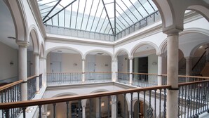 A spacious atrium with a glass ceiling, multiple levels, and a central staircase. - Petit Palace Marqués Santa Ana (Seville)