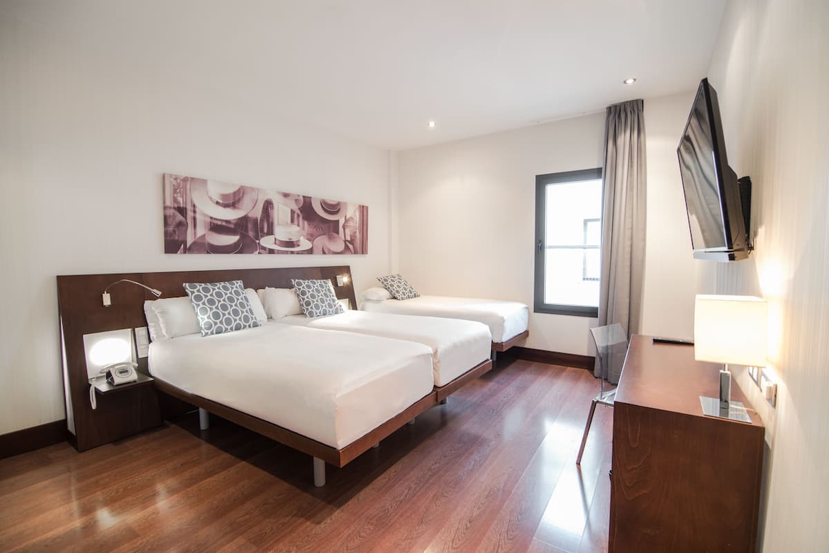 Une chambre d’hôtel avec un grand lit, un bureau, une télévision et une fenêtre avec des rideaux.