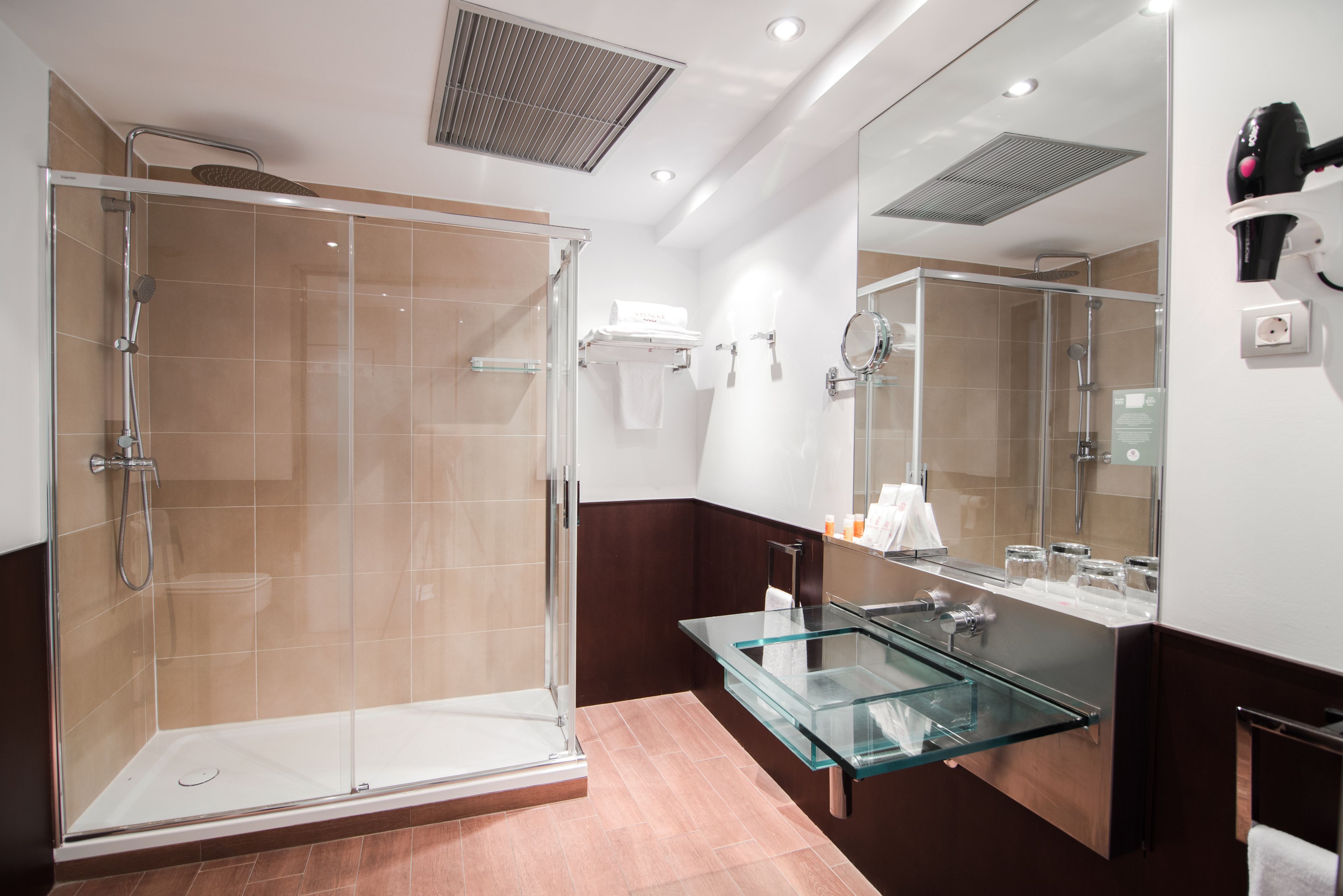 Un baño moderno con ducha envuelta en cristal, tocador de cristal y un espejo grande.