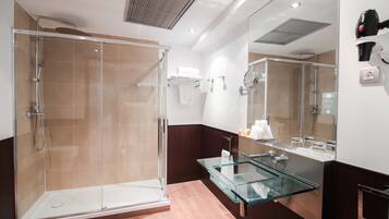 Un baño moderno con ducha envuelta en cristal, tocador de cristal y un espejo grande.