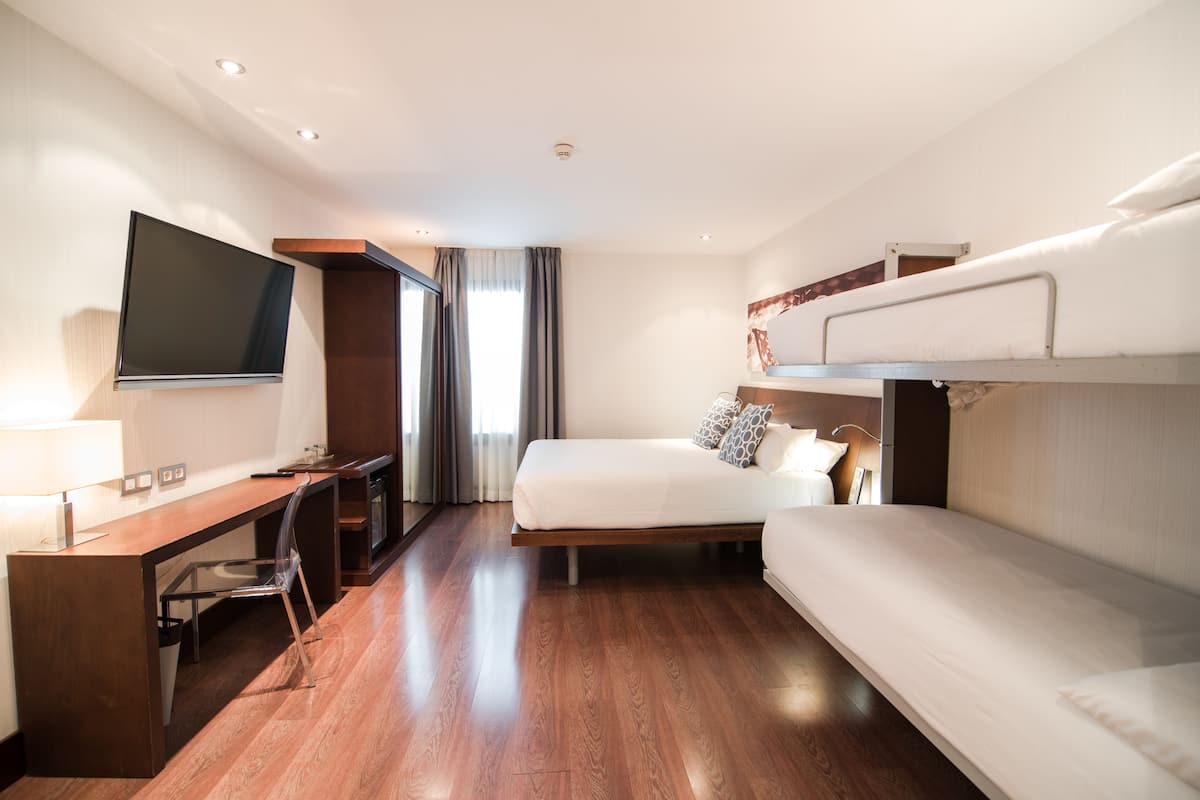 Une chambre d’hôtel moderne dotée d’un bureau en bois, d’un téléviseur à écran plat, d’un lit superposé et d’une grande fenêtre avec des rideaux.