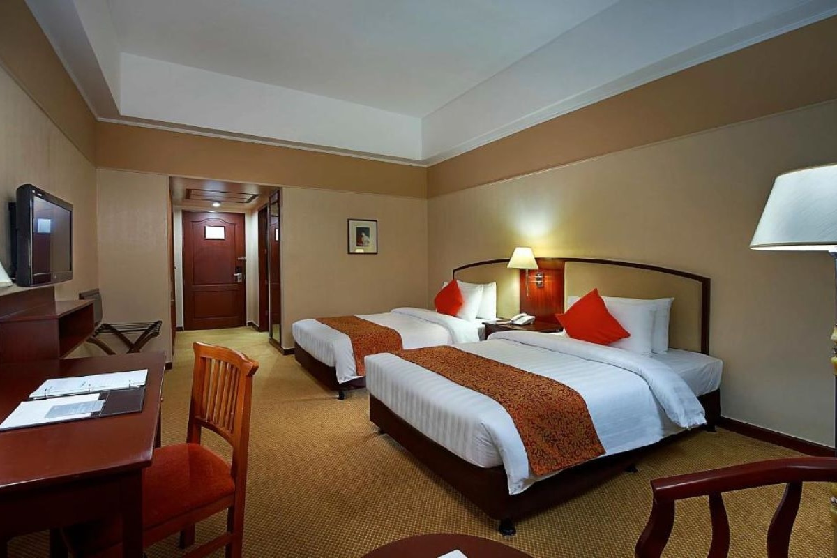 Een hotelkamer met twee bedden, een bureau, een stoel, een televisie en een deur.