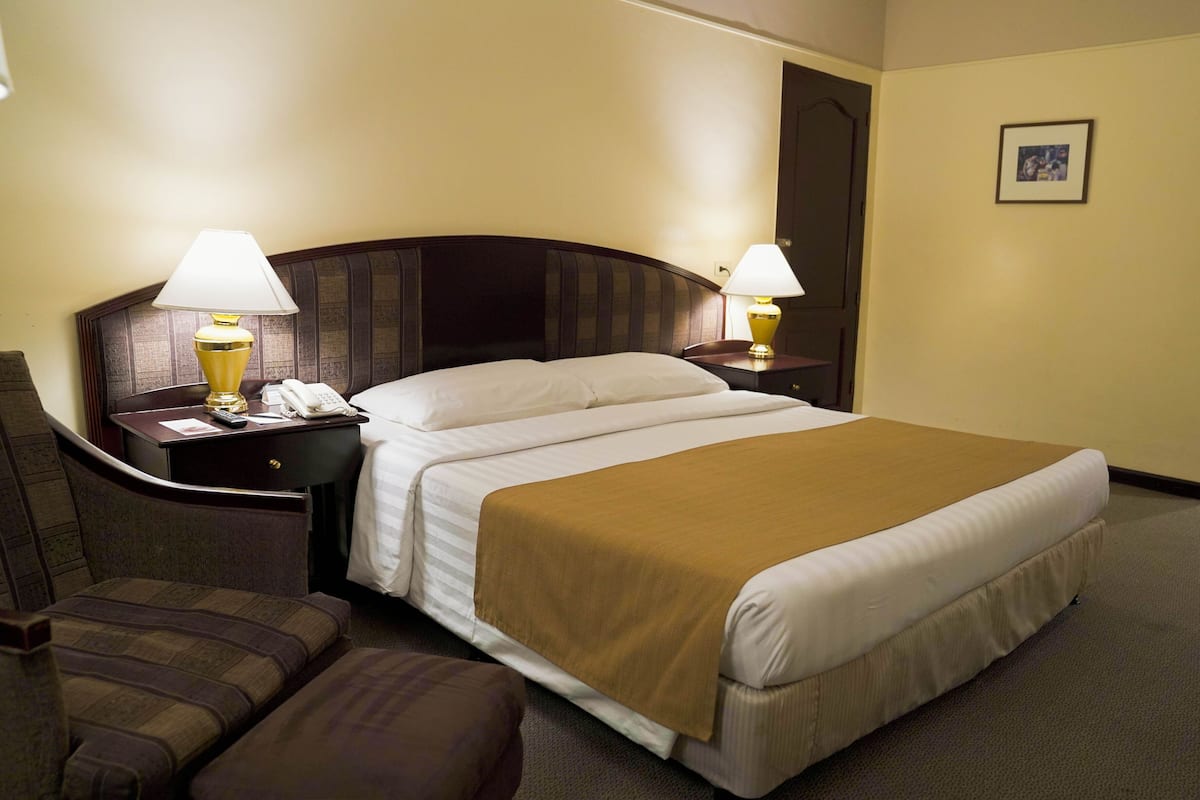 Een hotelkamer met een groot bed, twee nachtkastjes met lampen, een telefoon en een stoel.