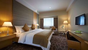 Habitación de hotel con una cama grande, dos mesitas de noche con lámparas, un escritorio con silla y un televisor de pantalla plana en la pared.