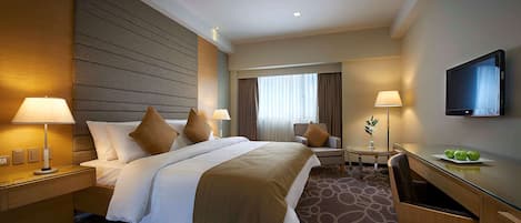 A hotel room with a large bed, two bedside tables with lamps, a desk with a chair, and a flat-screen TV on the wall.