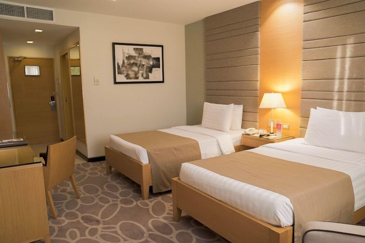 Een hotelkamer met twee bedden, een bureau en een stoel. Aan de muur hangt een schilderij en op het nachtkastje staat een lamp.