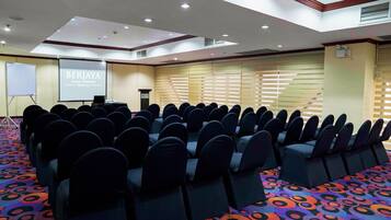 Un salón de conferencias con filas de sillas, una pantalla de proyección y un atril.