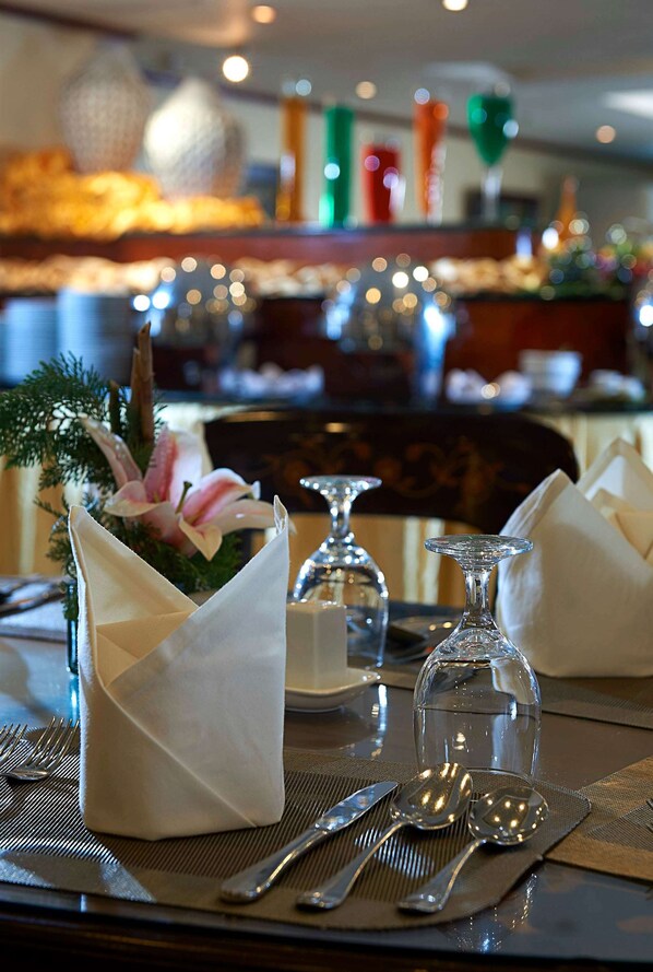 A dining table set with a water glass, two spoons, and a fork, with a napkin holder containing a flower. - Berjaya Makati Hotel (Makati)
