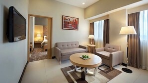 Habitación de hotel con sofá, dos sillones, una mesita de centro, televisor, un cuadro y una lámpara.