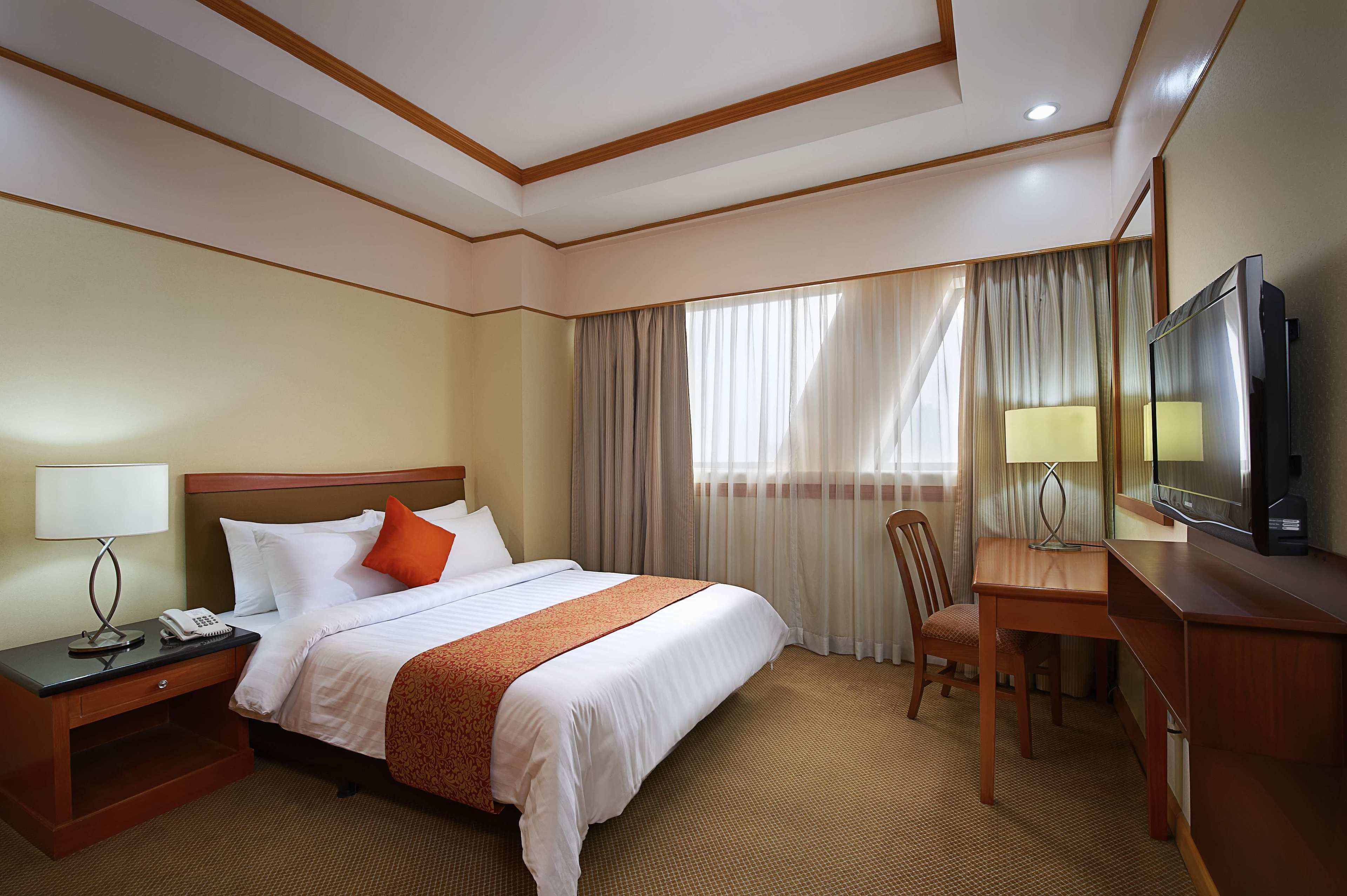 Una habitación de hotel con una cama grande, un escritorio con televisor, una silla y una mesita de noche con lámpara y teléfono.