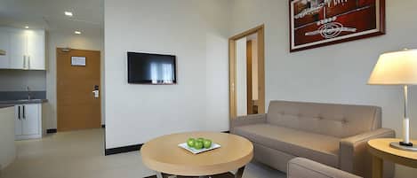Una habitación de hotel moderna con un sofá, una mesa redonda con manzanas, un televisor y un cuadro en la pared.