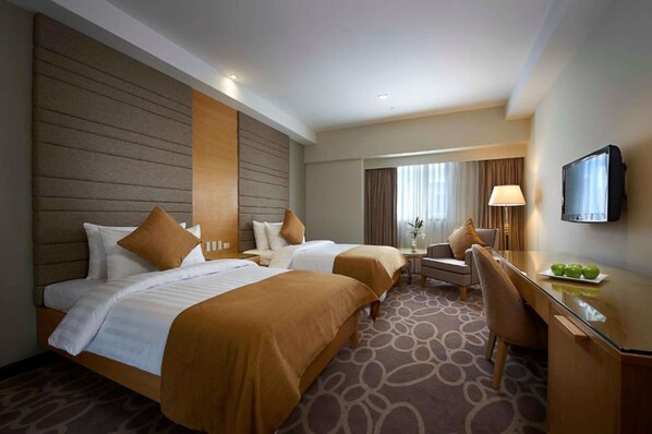 A hotel room with two beds, a desk, a chair, a TV, and a window with curtains. - Berjaya Makati Hotel (Makati)