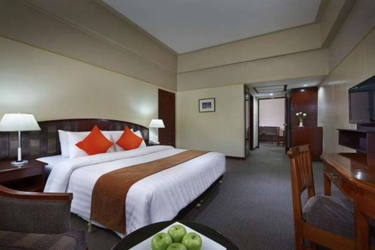 Een hotelkamer met een bed, twee bedlampen, een bureau met stoel, een televisie en een klein tafeltje met appels.
