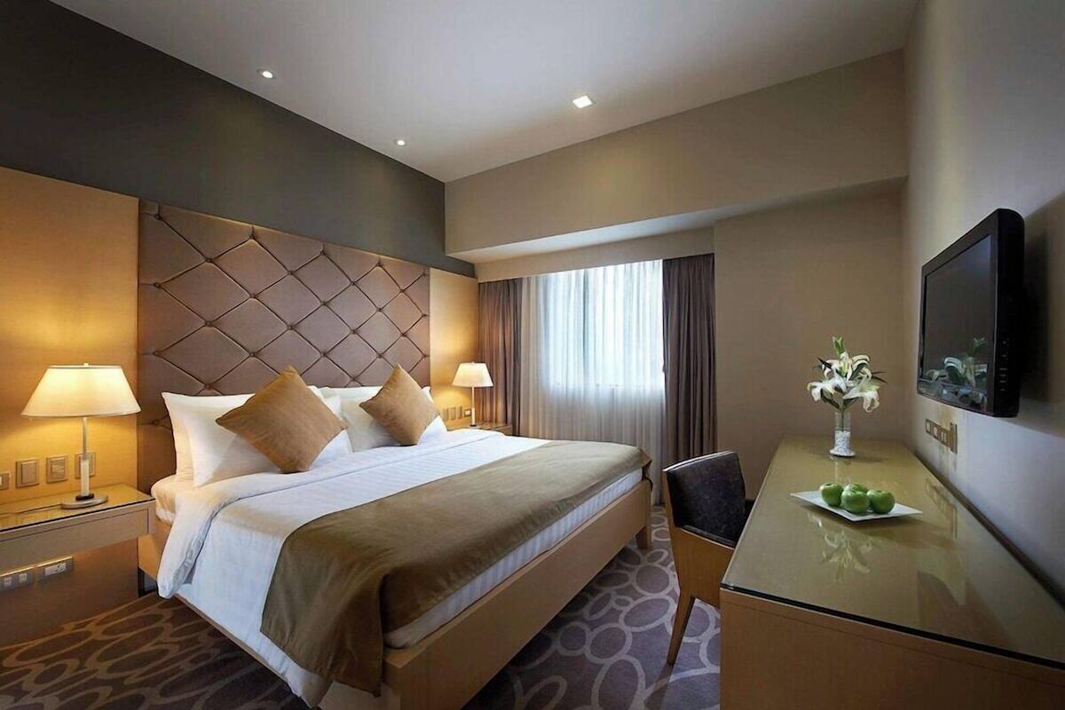 Een hotelkamer met een groot bed, nachtlampjes, een bureau met een televisie en een raam met gordijnen.