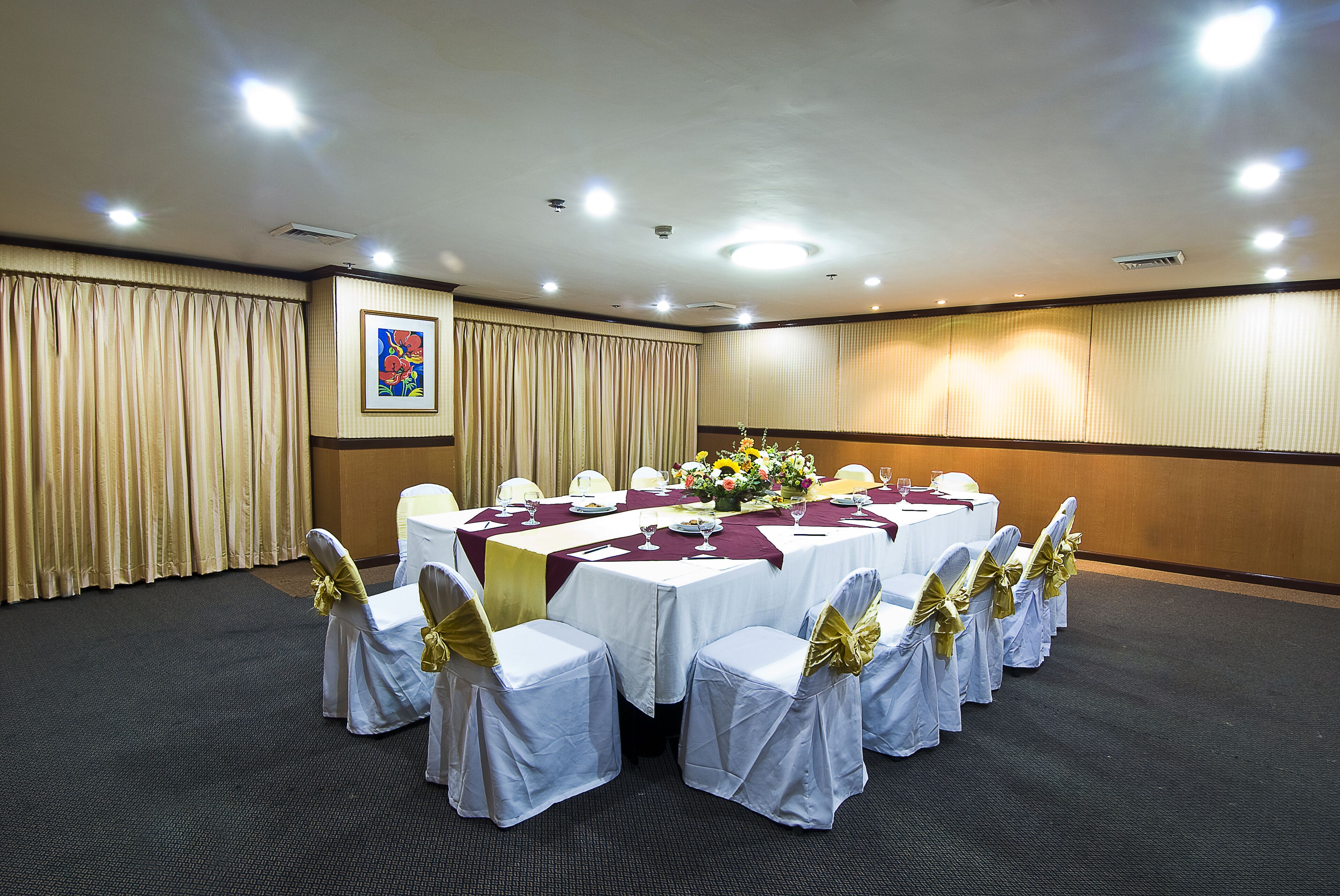 Ein Konferenzraum mit einem langen Tisch, weißen Stühlen mit goldenen Bändern und einer floralen Tischdekoration.