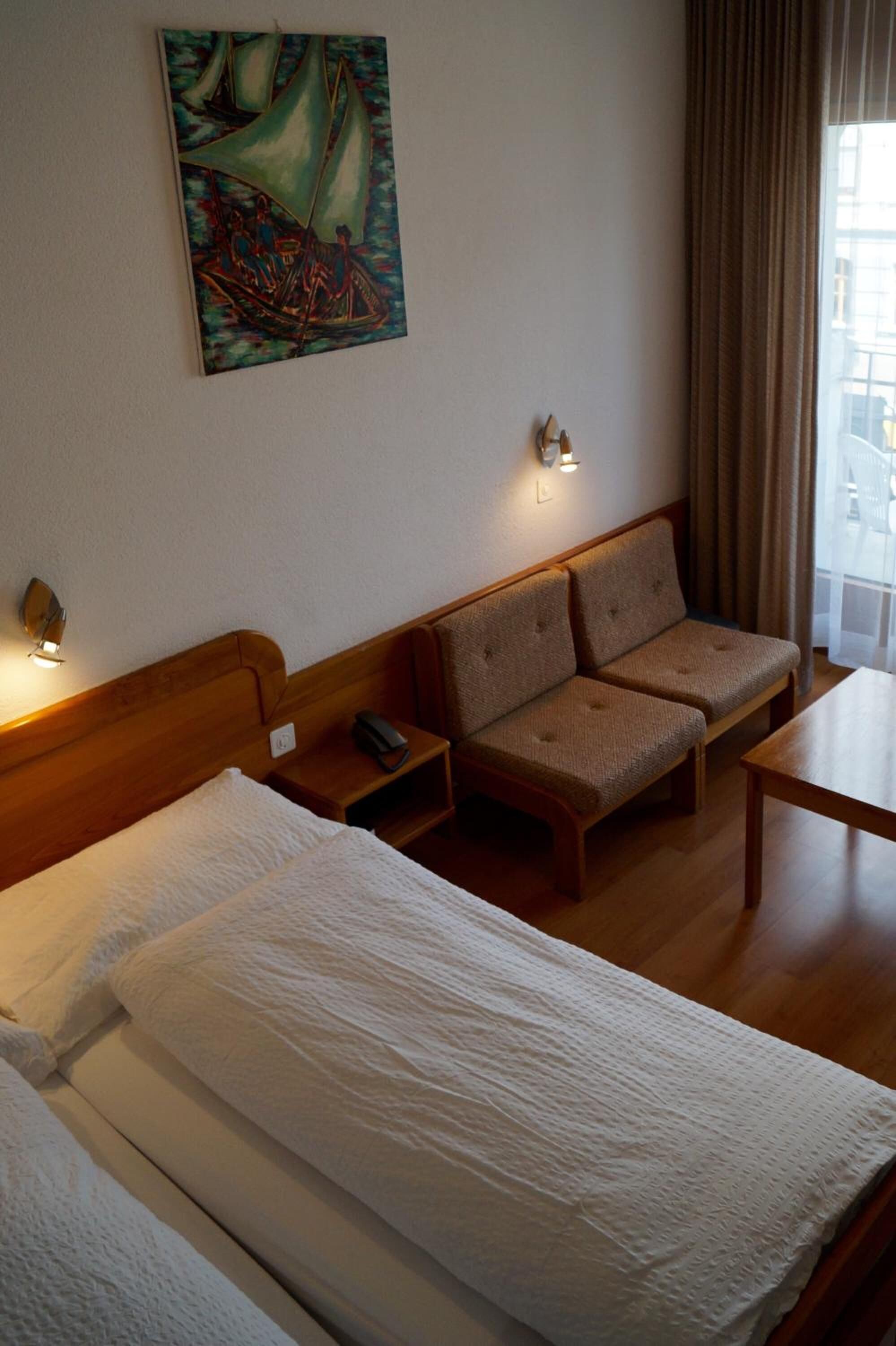 A hotel room with a bed, two sofas, a small table, a painting on the wall, and a window with curtains.