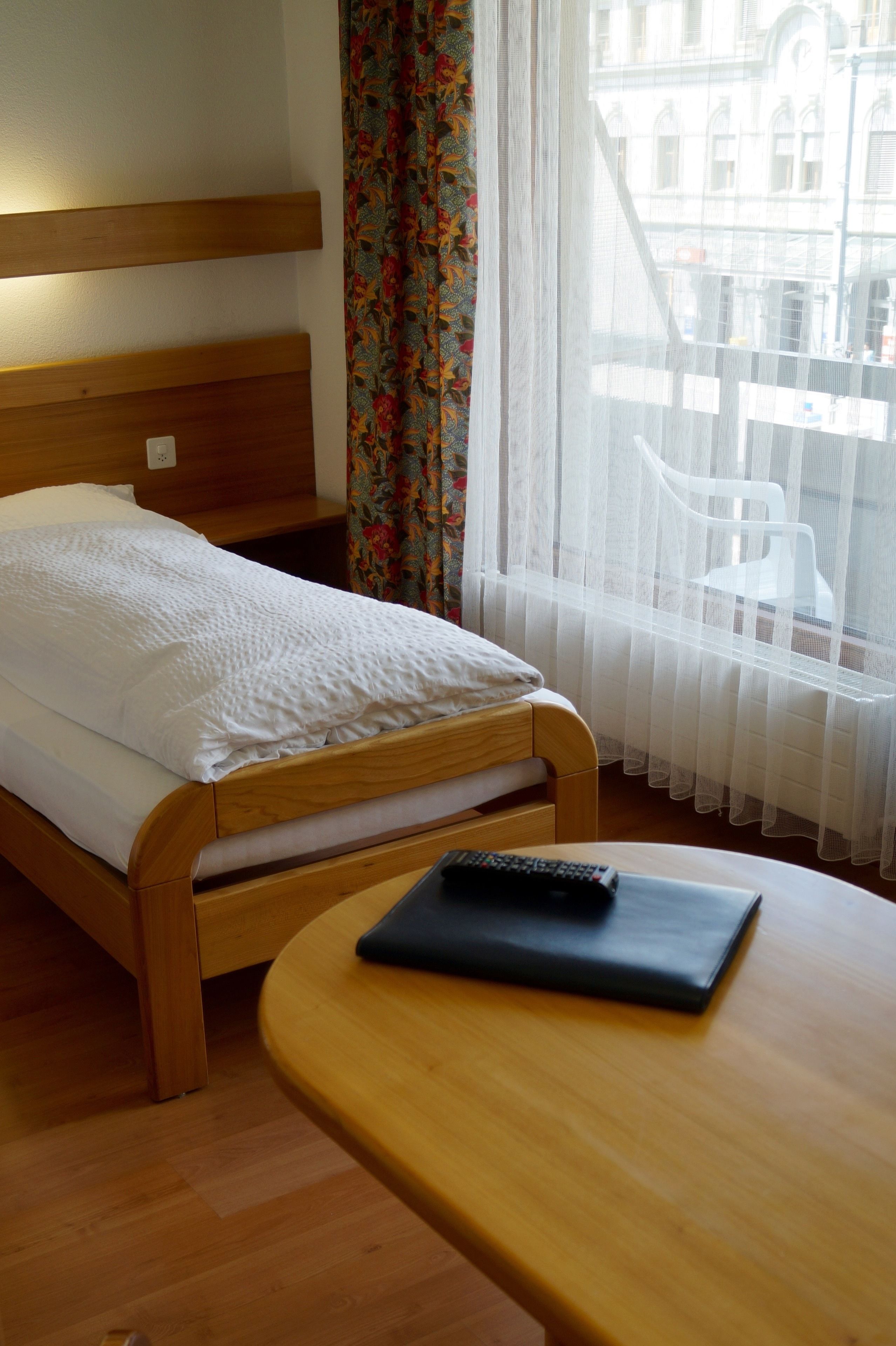 Ein hölzernes Bett mit weißer Matratze und einer Fernbedienung auf einem Holztisch.