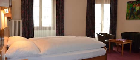 Una habitación de hotel con una cama grande, dos sillones, una mesita y un cuadro en la pared.