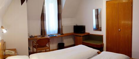 A hotel room with a bed, a desk with a chair, a television, a radiator, and a wardrobe.